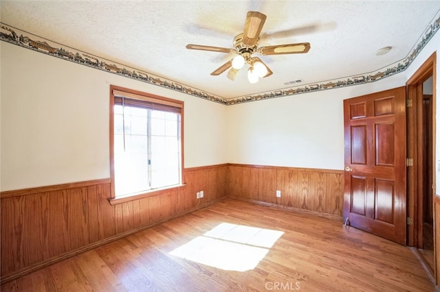 unfurnished room with ceiling fan, light hardwood / wood-style floors, a textured ceiling, and wood walls