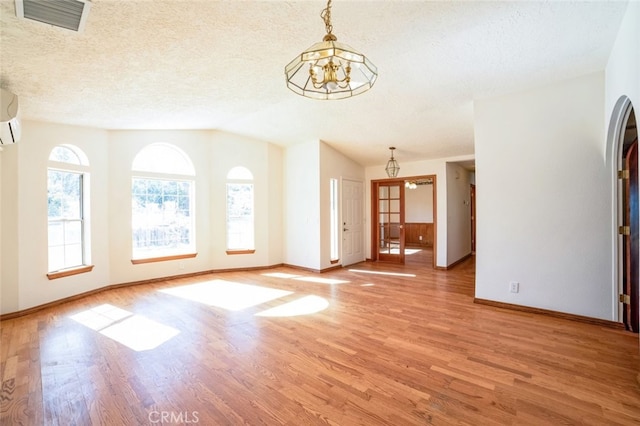 unfurnished living room featuring a chandelier, vaulted ceiling, a textured ceiling, and light wood-type flooring