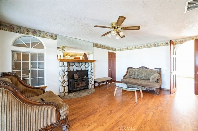 living area featuring ceiling fan, hardwood / wood-style flooring, a textured ceiling, and a wood stove