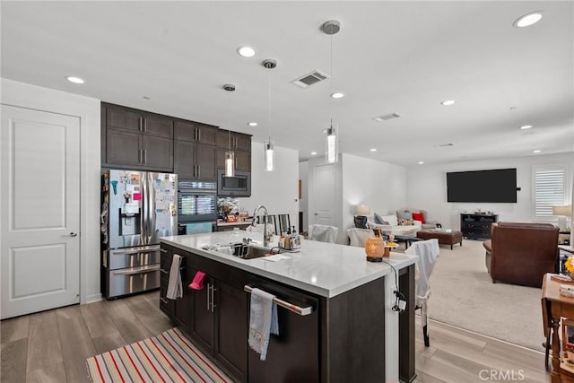 kitchen with appliances with stainless steel finishes, pendant lighting, an island with sink, sink, and light wood-type flooring