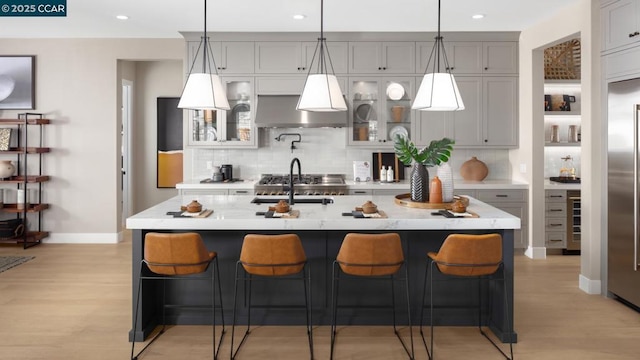 kitchen with pendant lighting, sink, light hardwood / wood-style flooring, gray cabinetry, and an island with sink