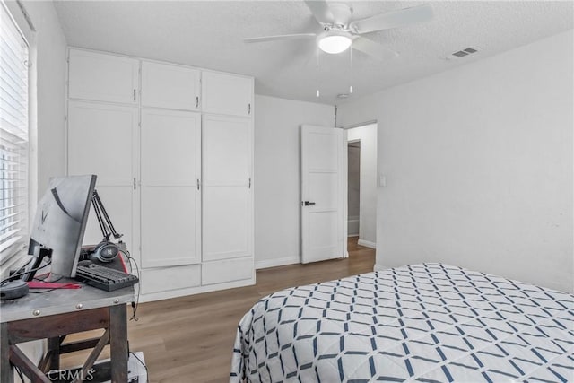 bedroom with ceiling fan, hardwood / wood-style floors, a textured ceiling, and a closet