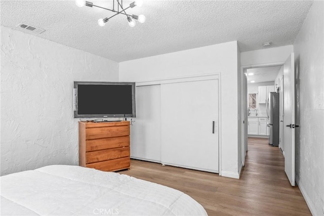 bedroom with stainless steel fridge, hardwood / wood-style flooring, a notable chandelier, a textured ceiling, and a closet