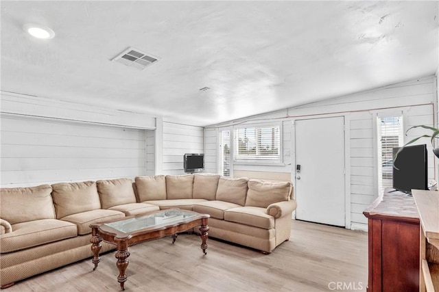 living room featuring lofted ceiling, light hardwood / wood-style flooring, and wood walls