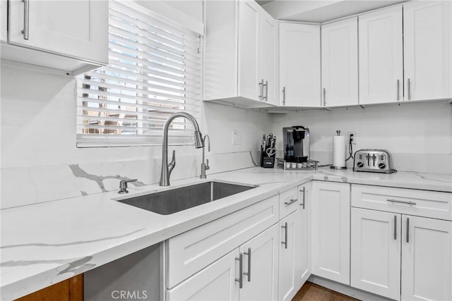 kitchen with white cabinetry, sink, and light stone countertops