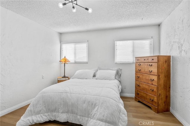 bedroom with a notable chandelier, light hardwood / wood-style floors, and a textured ceiling