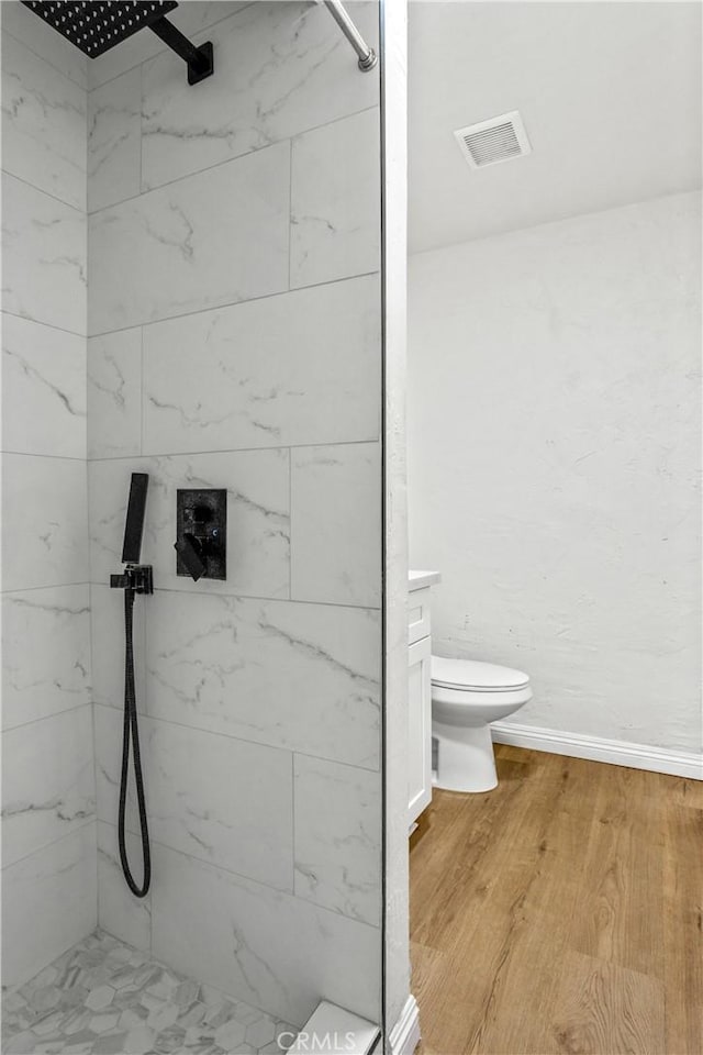 bathroom with tiled shower, toilet, and hardwood / wood-style floors