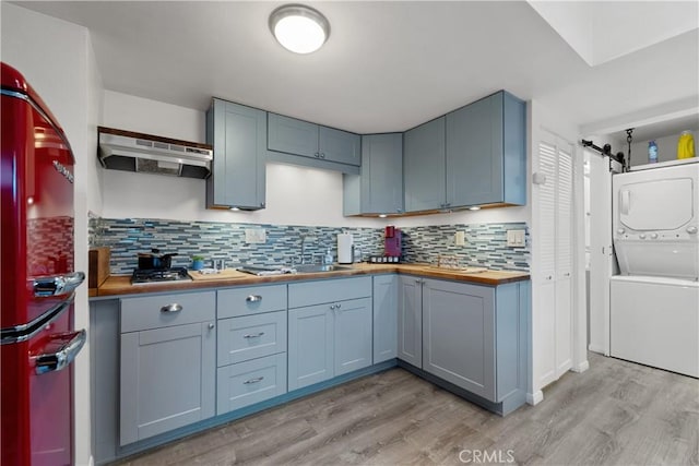 kitchen featuring sink, wooden counters, light wood-type flooring, stacked washing maching and dryer, and backsplash