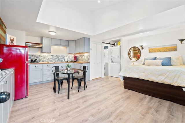 bedroom featuring fridge, stacked washer and clothes dryer, a barn door, and light hardwood / wood-style floors