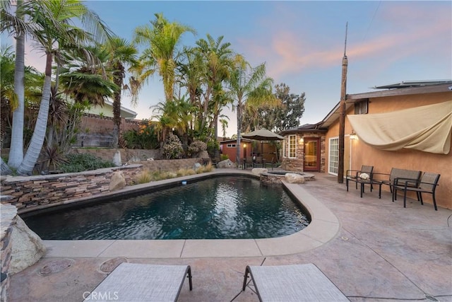 pool at dusk with a patio area and an in ground hot tub