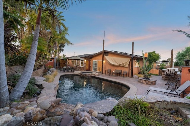 pool at dusk featuring a patio and an in ground hot tub