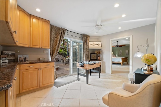 kitchen featuring light tile patterned floors, dark stone counters, and ceiling fan