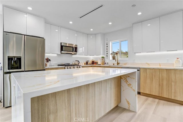 kitchen featuring a kitchen island, light stone countertops, white cabinets, and appliances with stainless steel finishes