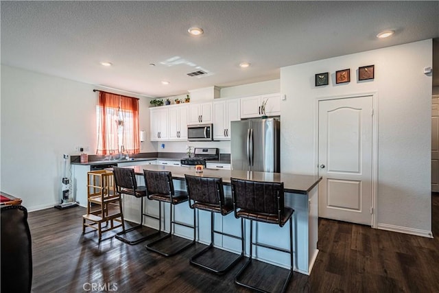 kitchen with stainless steel appliances, dark hardwood / wood-style floors, a center island, white cabinets, and a kitchen bar