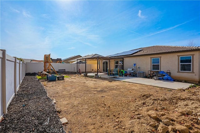 rear view of house featuring a playground, solar panels, and a patio area