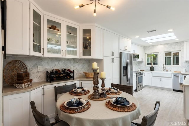 kitchen with sink, white cabinetry, a skylight, appliances with stainless steel finishes, and backsplash