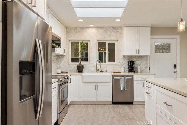 kitchen featuring appliances with stainless steel finishes, a skylight, sink, white cabinets, and hanging light fixtures