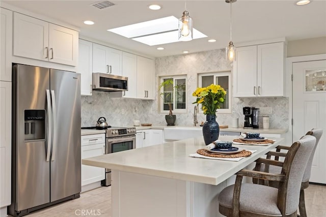 kitchen with sink, white cabinetry, a skylight, appliances with stainless steel finishes, and a kitchen breakfast bar