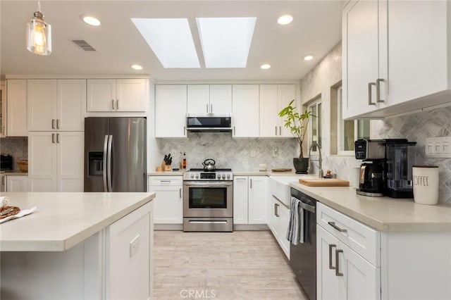 kitchen featuring white cabinetry, a skylight, hanging light fixtures, appliances with stainless steel finishes, and exhaust hood