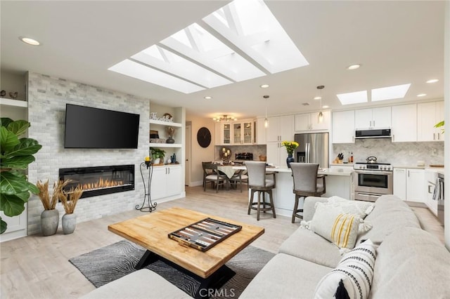 living room with a fireplace, a skylight, and light hardwood / wood-style floors