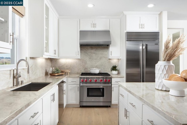 kitchen with sink, high quality appliances, light stone counters, extractor fan, and white cabinets