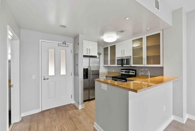 kitchen featuring white cabinetry, light stone counters, light hardwood / wood-style flooring, kitchen peninsula, and stainless steel appliances