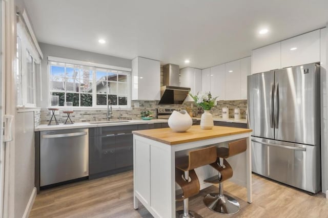 kitchen featuring sink, white cabinetry, stainless steel appliances, a center island, and wall chimney exhaust hood