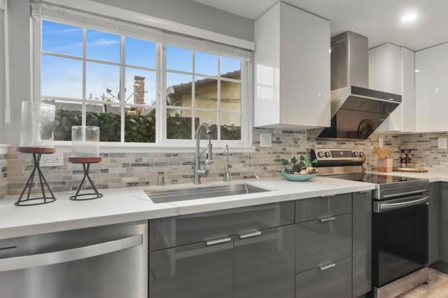 kitchen with wall chimney exhaust hood, sink, white cabinetry, light stone counters, and stainless steel appliances