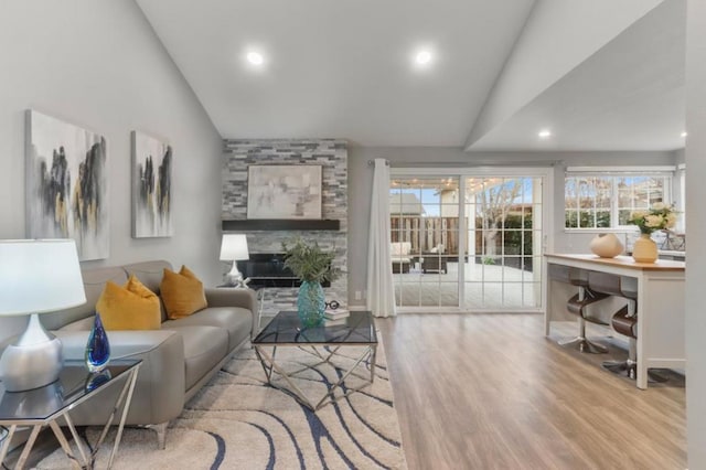 living room featuring a stone fireplace, vaulted ceiling, and light wood-type flooring