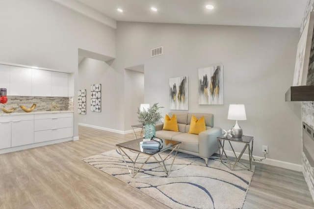 living room with high vaulted ceiling, a fireplace, and light hardwood / wood-style flooring