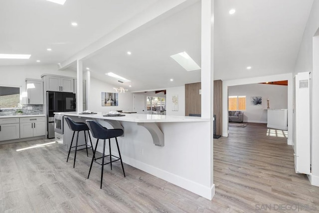 kitchen with vaulted ceiling with skylight, plenty of natural light, a breakfast bar, and gray cabinetry