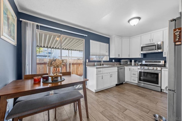 kitchen with appliances with stainless steel finishes, white cabinetry, sink, light wood-type flooring, and a textured ceiling