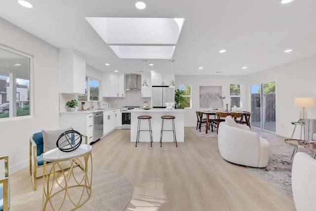 kitchen featuring white cabinetry, hanging light fixtures, appliances with stainless steel finishes, a kitchen island, and wall chimney range hood