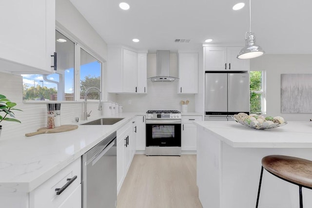 kitchen with sink, white cabinetry, stainless steel appliances, decorative light fixtures, and wall chimney exhaust hood