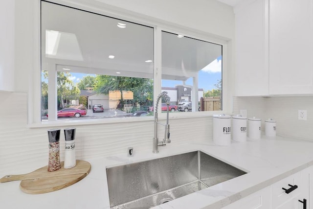 interior details with light stone counters, backsplash, sink, and white cabinets