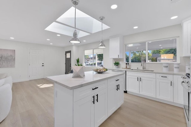 kitchen featuring white cabinetry, a skylight, sink, and hanging light fixtures