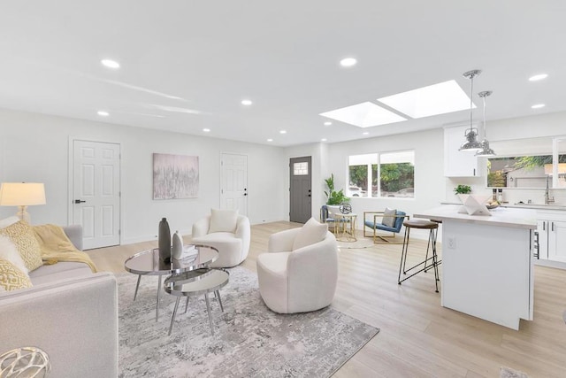 living room with a skylight, sink, and light hardwood / wood-style flooring