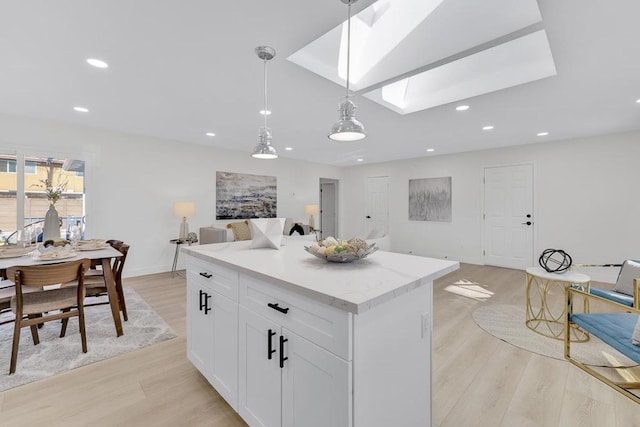 kitchen featuring a center island, a skylight, light wood-type flooring, pendant lighting, and white cabinets