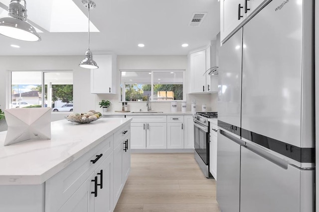 kitchen with sink, white cabinetry, fridge, stainless steel range with gas stovetop, and pendant lighting