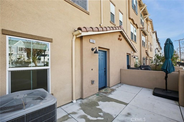 view of exterior entry with a patio and central air condition unit