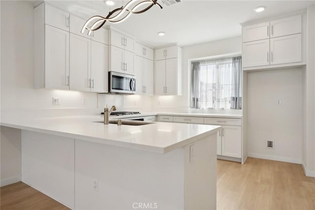 kitchen with white cabinetry, hanging light fixtures, kitchen peninsula, and appliances with stainless steel finishes