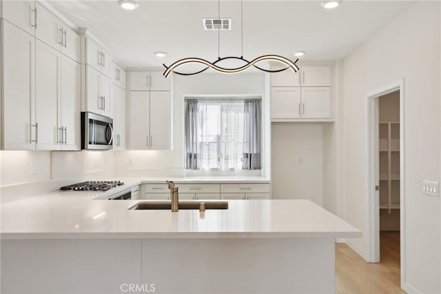 kitchen with sink, kitchen peninsula, pendant lighting, light hardwood / wood-style floors, and white cabinets