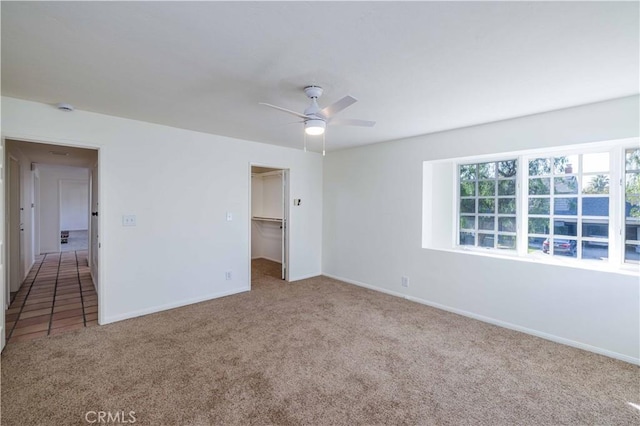 unfurnished bedroom with light carpet, a spacious closet, a closet, and ceiling fan