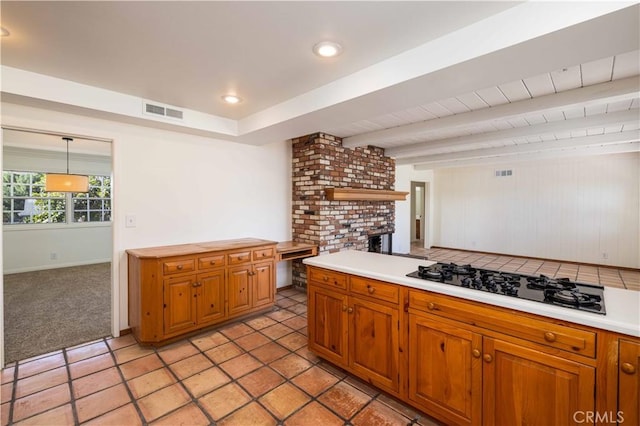 kitchen featuring gas cooktop, beam ceiling, light carpet, a brick fireplace, and decorative light fixtures