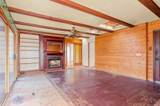 unfurnished living room featuring ceiling fan, a fireplace, beam ceiling, and wood walls