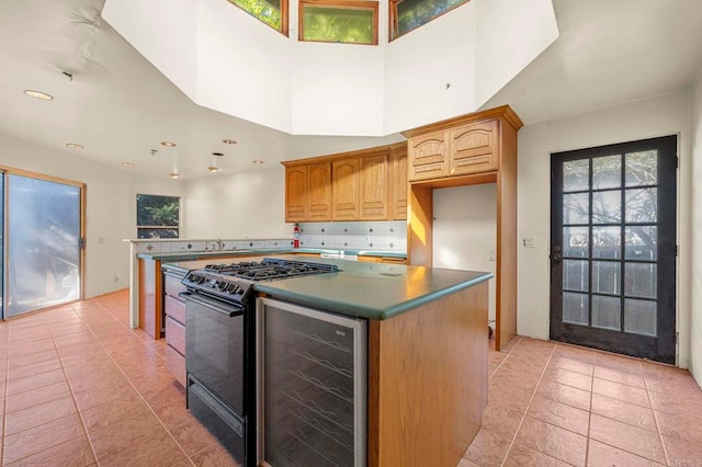 kitchen featuring wine cooler, a center island, light tile patterned floors, black range with gas stovetop, and a towering ceiling