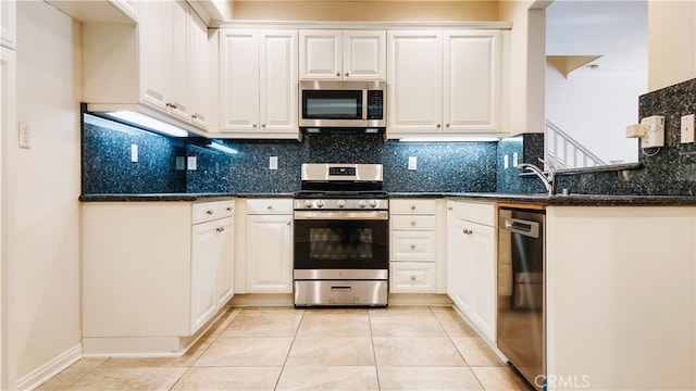 kitchen with stainless steel appliances, dark stone countertops, white cabinets, and backsplash