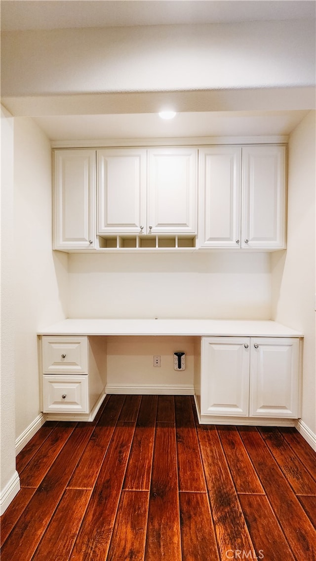 unfurnished office featuring built in desk and dark hardwood / wood-style floors