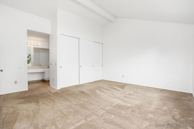 unfurnished bedroom featuring ensuite bathroom, carpet floors, a closet, and vaulted ceiling with beams