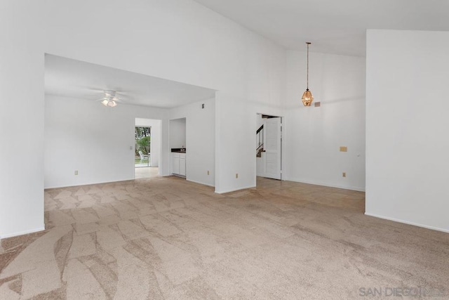 unfurnished living room with ceiling fan, high vaulted ceiling, and light carpet